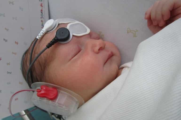 This shows a newborn with a headset and eeg wires on her head