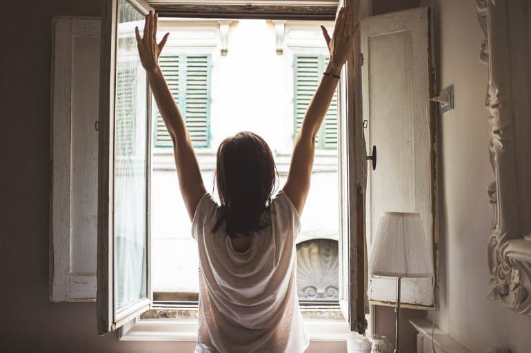 This shows a woman stretching by an open window on a sunny morning