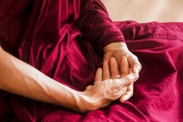 This shows an older person's hands crossed in meditation