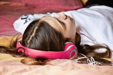 This shows a young girl laying down with headphones on