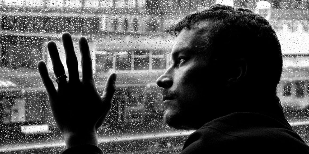 This shows a depressed looking man looking out of a rainy window