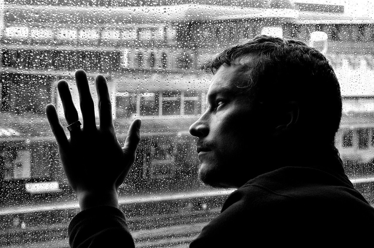 This shows a depressed looking man looking out of a rainy window