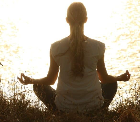 This shows a woman meditating by a river
