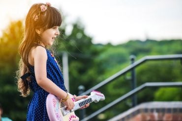 This shows a little girl singing and playing a toy guitar