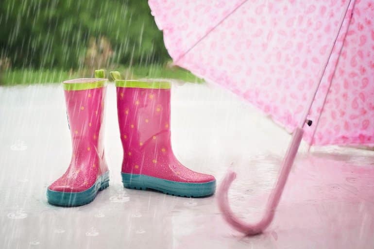 Isso mostra as botas de chuva rosa de uma menina e um guarda-chuva rosa.