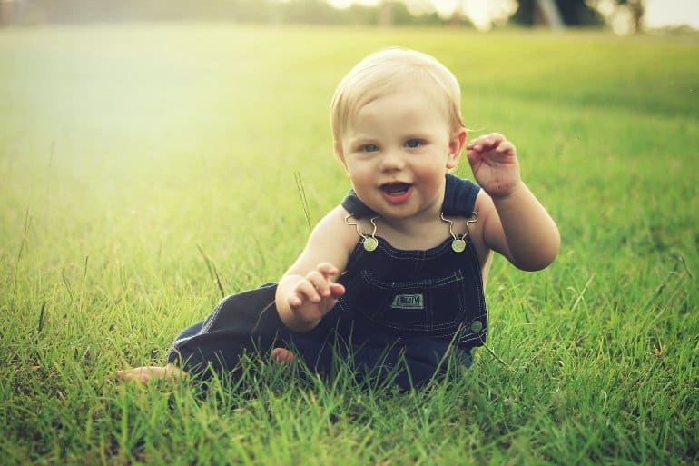 This shows a happy baby sitting in a field