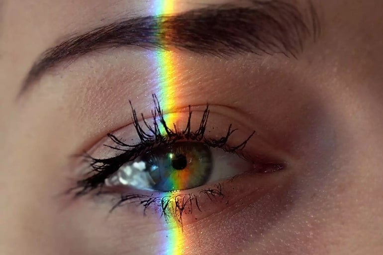 This shows a woman's eye with a rainbow light beam over it