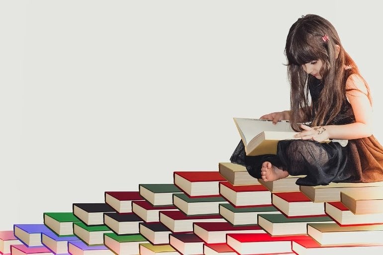 This shows a little girl reading on top of a stack of books