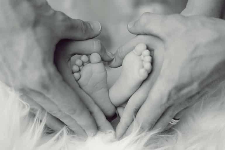 Isso mostra os pés de um recém-nascido sendo embalados pelas mãos de uma mãe e de um pai