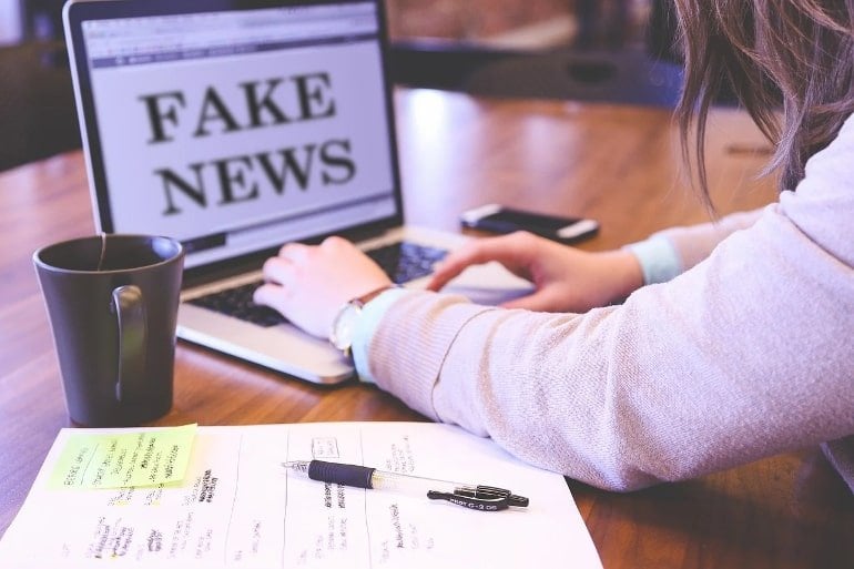 This shows a woman looking at a computer with the words "fake news" written on it