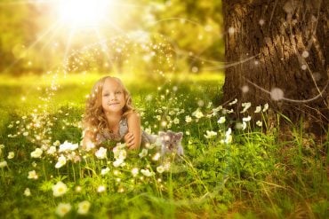 This shows a young girl sitting under a tree in the sunshine