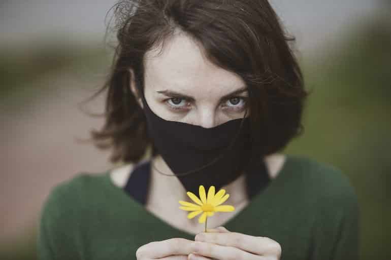 This shows a woman in a facemask holding a flower