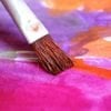 This shows a paintbrush applying bright pink paint to canvas