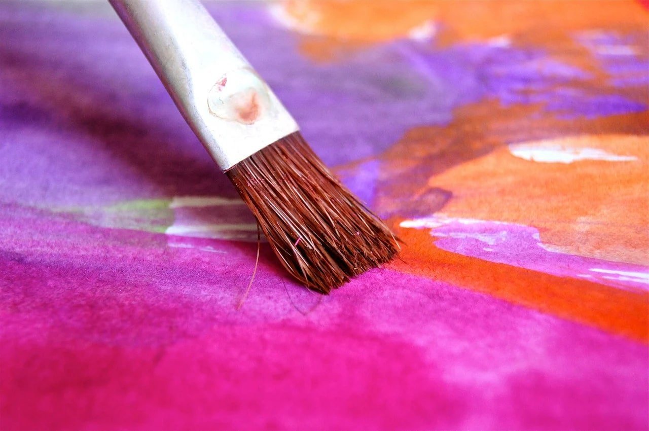 This shows a paintbrush applying bright pink paint to canvas