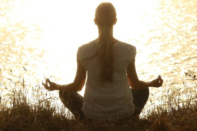 This shows a woman meditating by a river