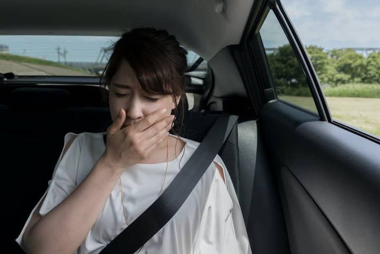 This shows a woman covering her mouth, sitting in the back of a car
