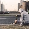This shows a young man sitting at the side of a road with a bottle of beer