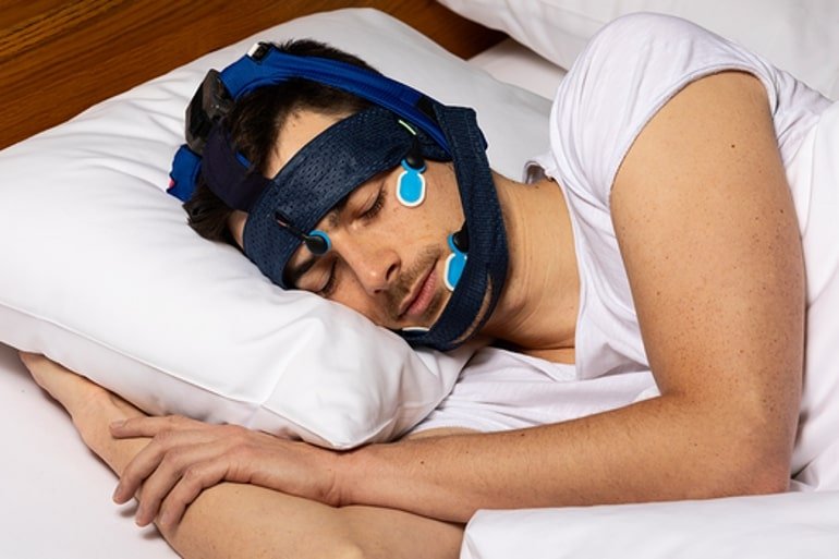 This shows a man sleeping with the SleepLoop system on his head