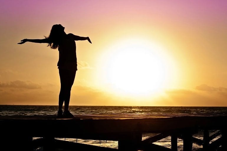 This shows a happy woman with her arms outstretched at sunset
