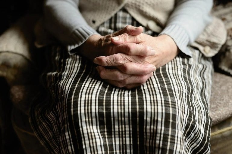 Dies zeigt eine ältere Dame mit über den Knien gekreuzten Händen