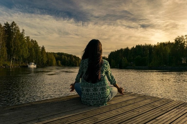 Esto muestra a una mujer sentada pacíficamente junto a un lago.