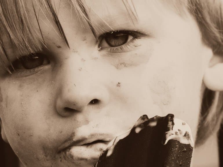 This shows a young child eating an ice cream bar with his face covered in chocolate