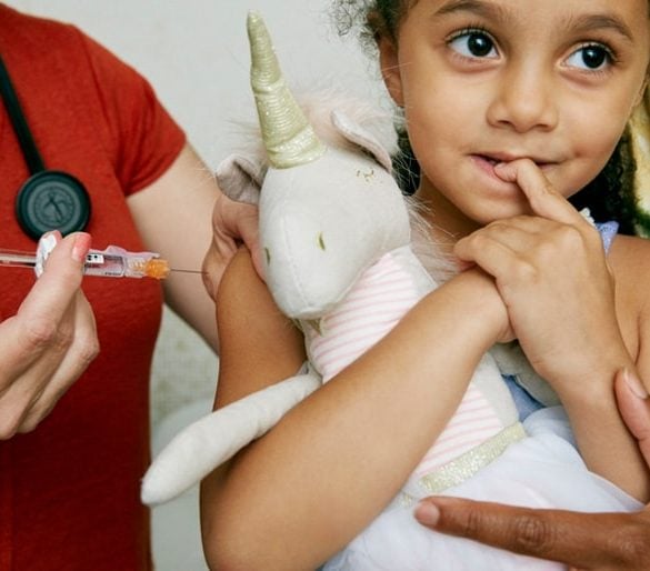 This shows a young girl getting vaccinated while holding a plushy unicorn toy