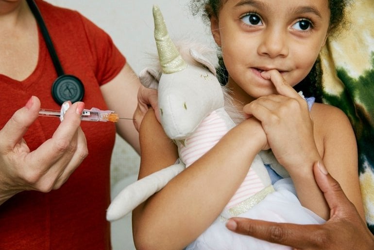 This shows a young girl getting vaccinated while holding a plushy unicorn toy