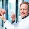 This shows the researcher holding a model of a brain and a syringe