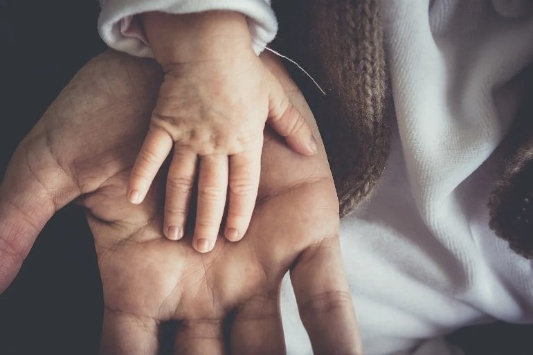 This shows a baby's hand in an adults hand