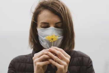 This shows a woman in a facemask holding a flower