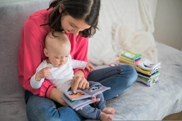 This shows a mom reading a book with her infant