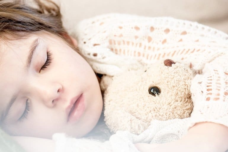 This shows a little girl sleeping with her teddy bear