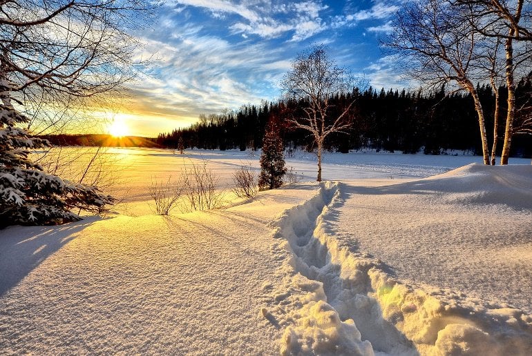This shows a walking track through a snowy field surrounded by trees and a gorgeous sun set