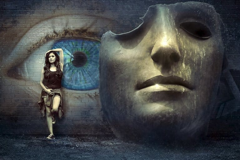 This shows a woman standing next to a mask and a painting of an eye