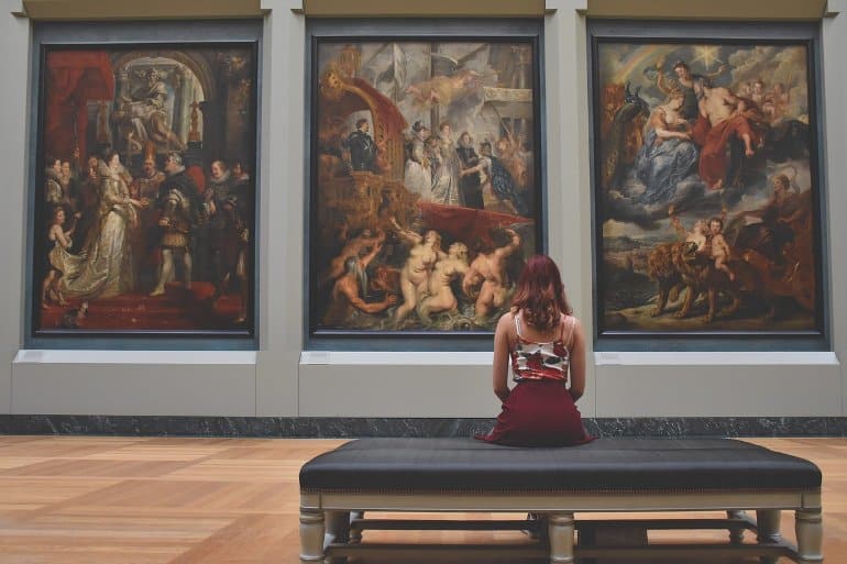 Photo of a woman sitting in a art gallery looking a three large paintings