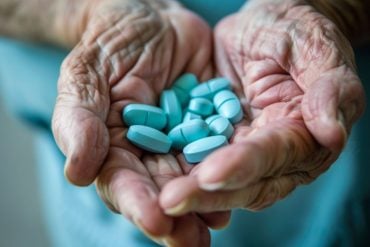 This shows blue pills in an old man's hand.