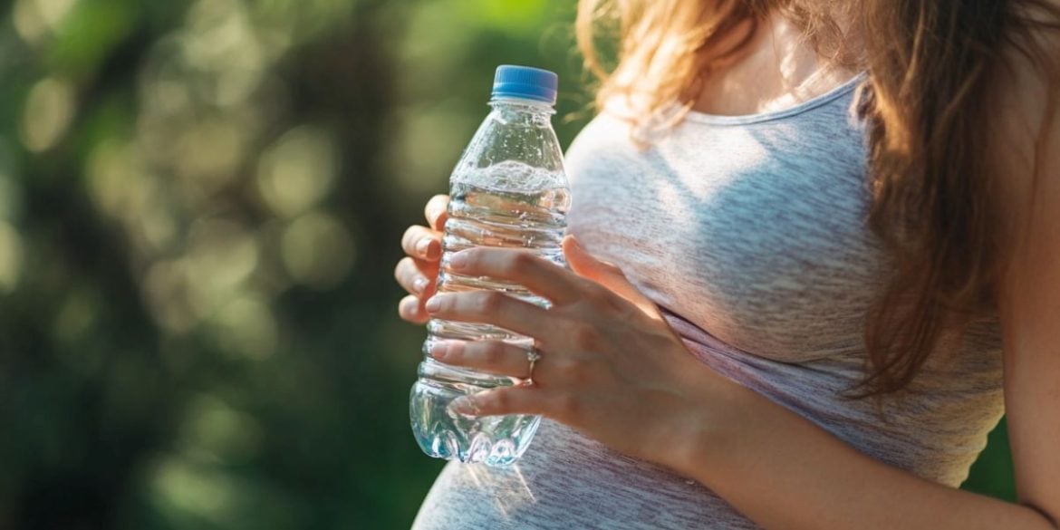 This shows a pregnant woman holding a bottle of water.