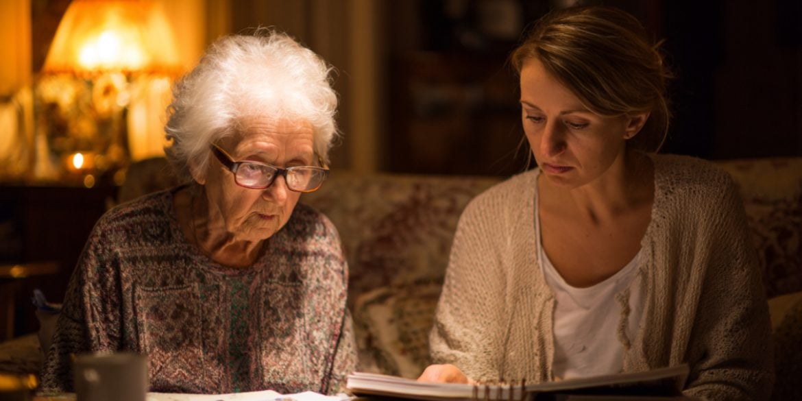 This shows an older woman looking through a photo album with her caregiver.
