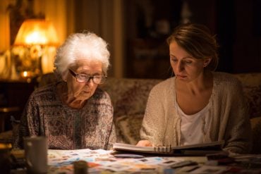 This shows an older woman looking through a photo album with her caregiver.