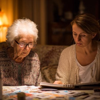This shows an older woman looking through a photo album with her caregiver.