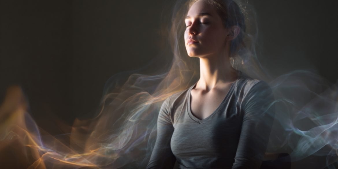 This shows a woman in a meditative pose with a small device on her ear. She looks at peace and is surrounded by waves.