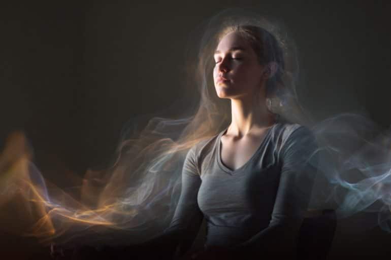 This shows a woman in a meditative pose with a small device on her ear. She looks at peace and is surrounded by waves.