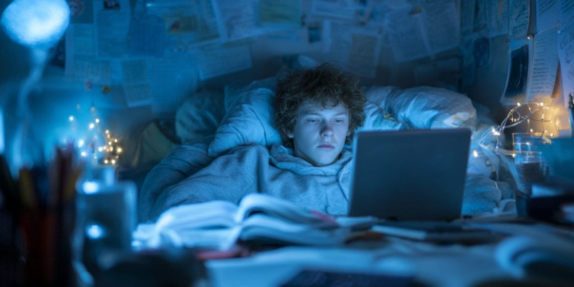 This shows a teen in bed, awake and looking at a computer late at night.