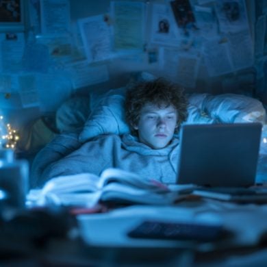 This shows a teen in bed, awake and looking at a computer late at night.