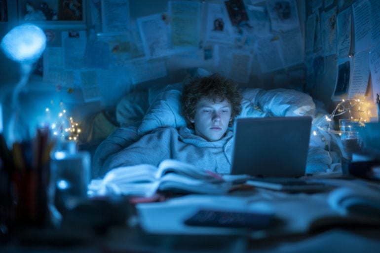 This shows a teen in bed, awake and looking at a computer late at night.