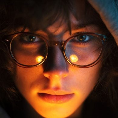 This shows a woman wearing glasses. The light around her is dim.