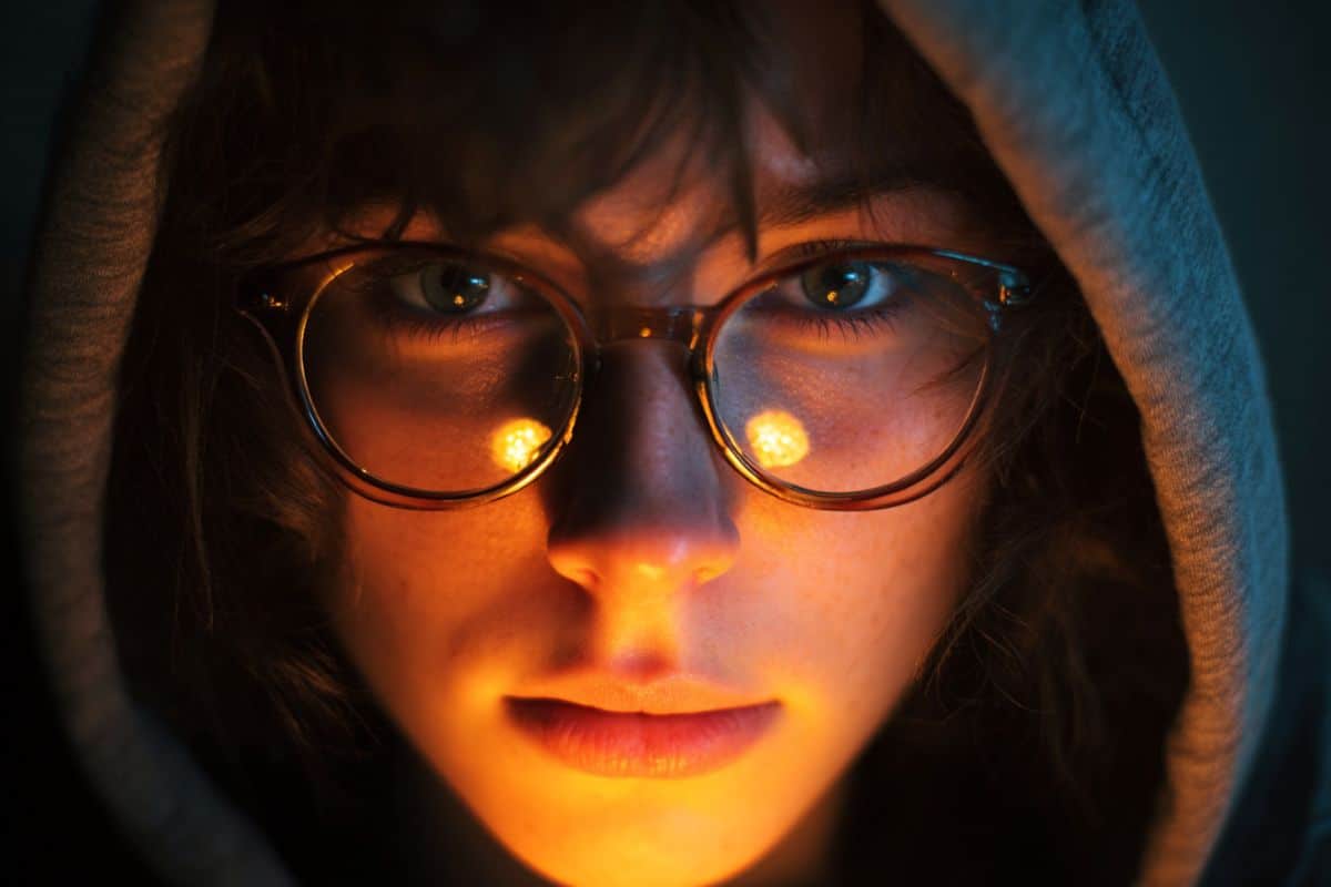 This shows a woman wearing glasses. The light around her is dim.