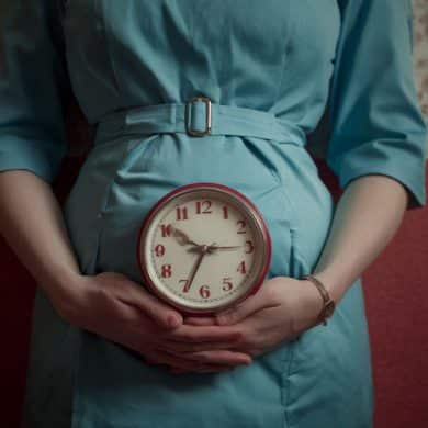 This shows a pregnant woman holding a clock.