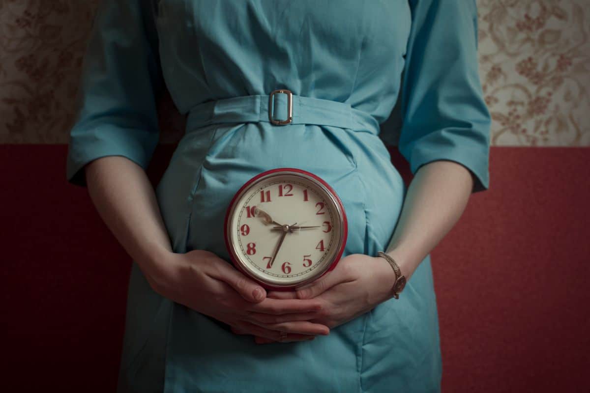 This shows a pregnant woman holding a clock.